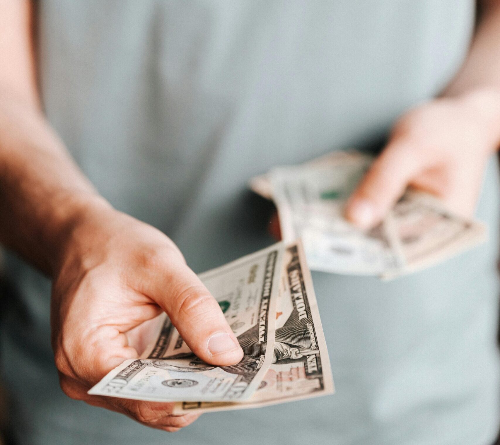 Close-up of an unrecognizable man holding dollar bills with a blurred background indoors.
